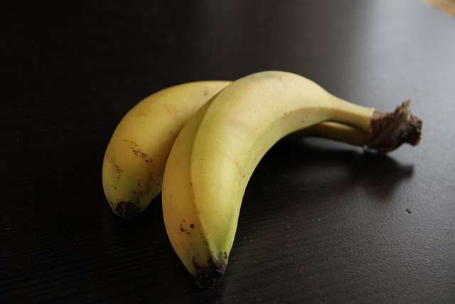 "Duas pequenas bananas-maçã ao lado de uma taça de fruta, ilustrando uma porção ideal para o lanche das crianças."