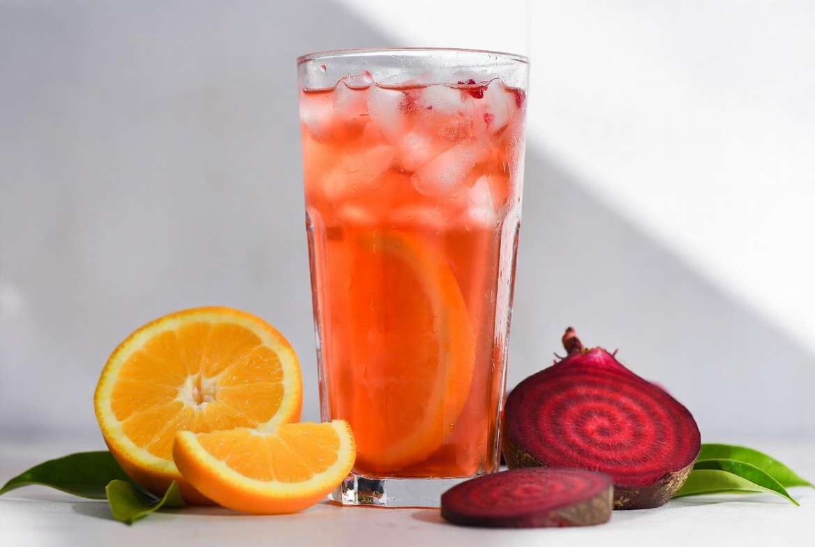 "Suco de laranja com beterraba gelado num copo de vidro com gotas de condensação e cubos de gelo."