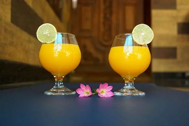 "Suco de manga em um copo decorado com uma fatia da fruta na borda e gelo."