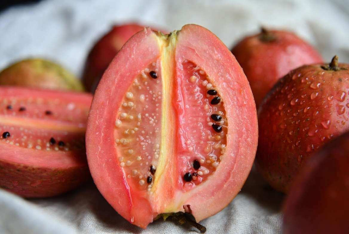 Uma goiaba vermelha fresca cortada ao meio exibe sua polpa vibrante e sementes sobre uma superfície limpa.