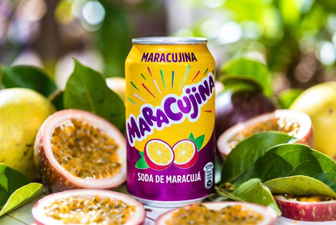 Uma lata decorativa com a ilustração de suco de maracugina, posicionada ao lado da fruta fresca aberta com sementes aparentes.