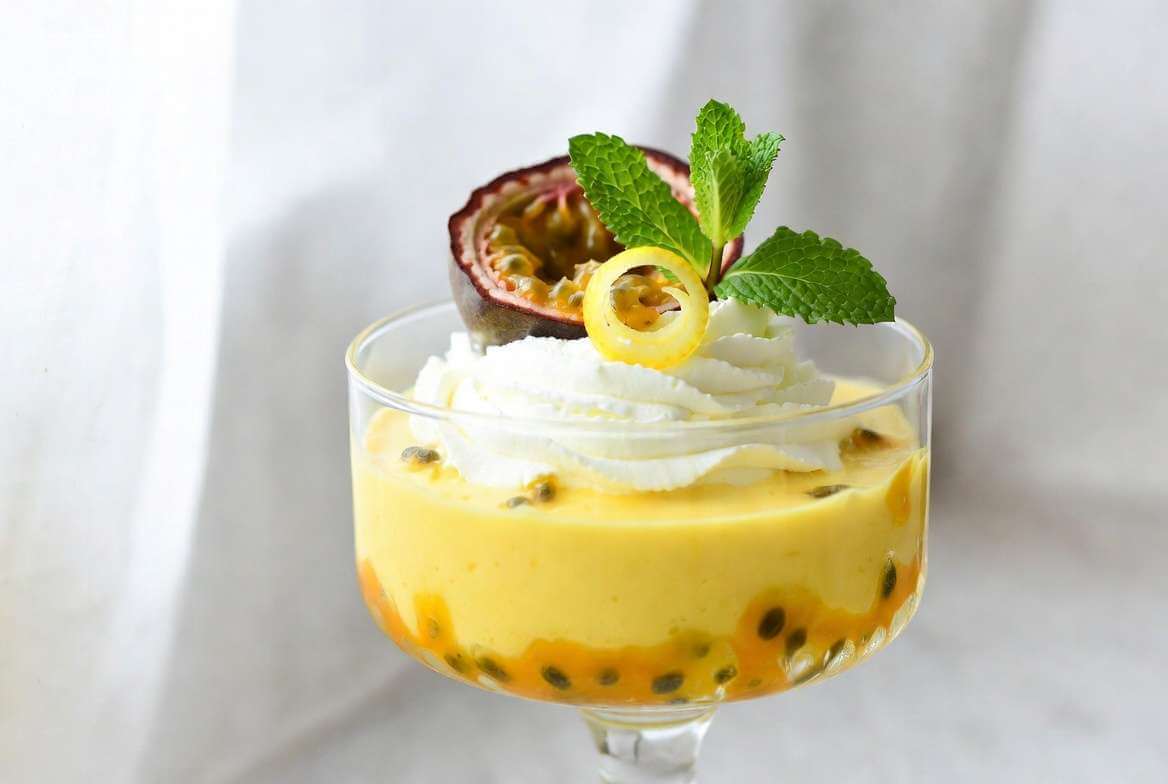  Uma travessa de vidro grande cheia de mousse de maracujá cremosa com calda brilhante e sementes por cima sobre uma mesa de madeira.