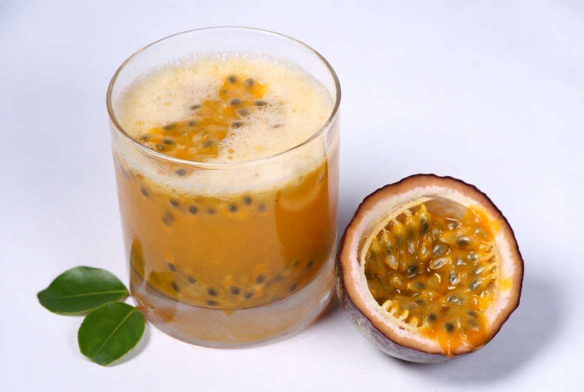 Um copo de vidro transparente cheio de suco de maracujá bem gelado com uma rodela de limão decorando a borda sobre uma mesa de madeira.