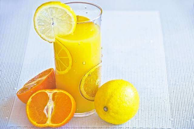 Suco de Limão: Benefícios, Mitos e Como Consumir 3 Copo de vidro transparente com suco de limão e uma rodela de limão cortada ao meio na borda, sobre uma superfície limpa.