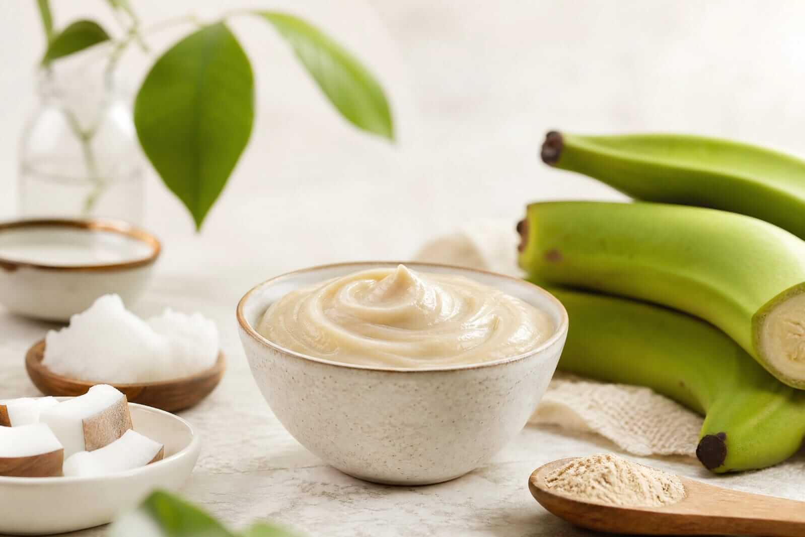 Biomassa de banana verde cremosa, de cor bege clara, armazenada em um pote de vidro transparente sobre uma bancada de cozinha