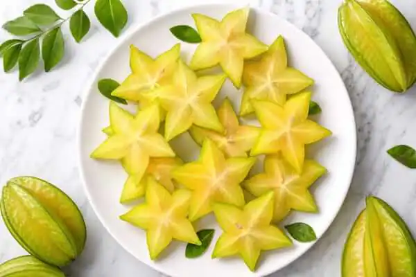 Grávida Pode Comer Carambola? Benefícios, Riscos e Cuidados 2 Carambola inteira amarela e fatias cortadas em formato de estrela dispostas sobre uma mesa de madeira.