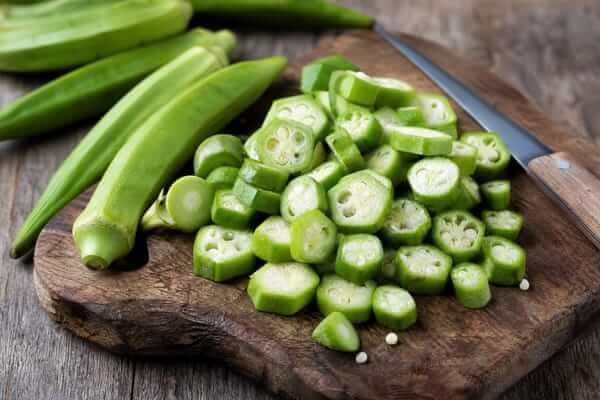 Guia do Quiabo: Cultivo, Receitas e Variedades Imperdíveis 2 Quiabos inteiros verdes e frescos ao lado de quiabos fatiados em rodelas sobre uma tábua de madeira na cozinha.
